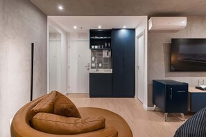 Ein modernes Wohnzimmer mit einer gebogenen Couch, einer Küchenzeile mit dunklen Schränken und einem flachbildfernseher an der Wand.