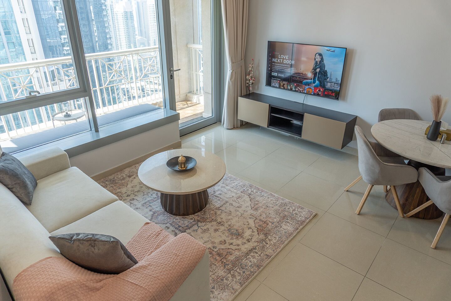 Un salon moderne comprenant un canapé, une table basse et un coin repas, un téléviseur fixé au mur, ainsi qu’un balcon offrant une vue sur la ville.