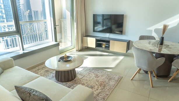 Een moderne woonkamer met een bank, een ronde salontafel, een televisie en een eethoek met tafel en stoelen.