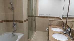 Een badkamer met een douchecabine van glas, een bad en twee wastafels met spiegels.