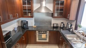 Een moderne keuken met donkere houten kastjes, roestvrijstalen apparatuur, een inbouwoven, een koffiezetapparaat en een spoelbak.