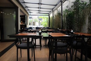 An indoor dining area with tables and chairs, a glass wall with a view, and a plant wall. - #BC1006 | Cyclinn Bela Cintra Jardins (Bela Cintra)