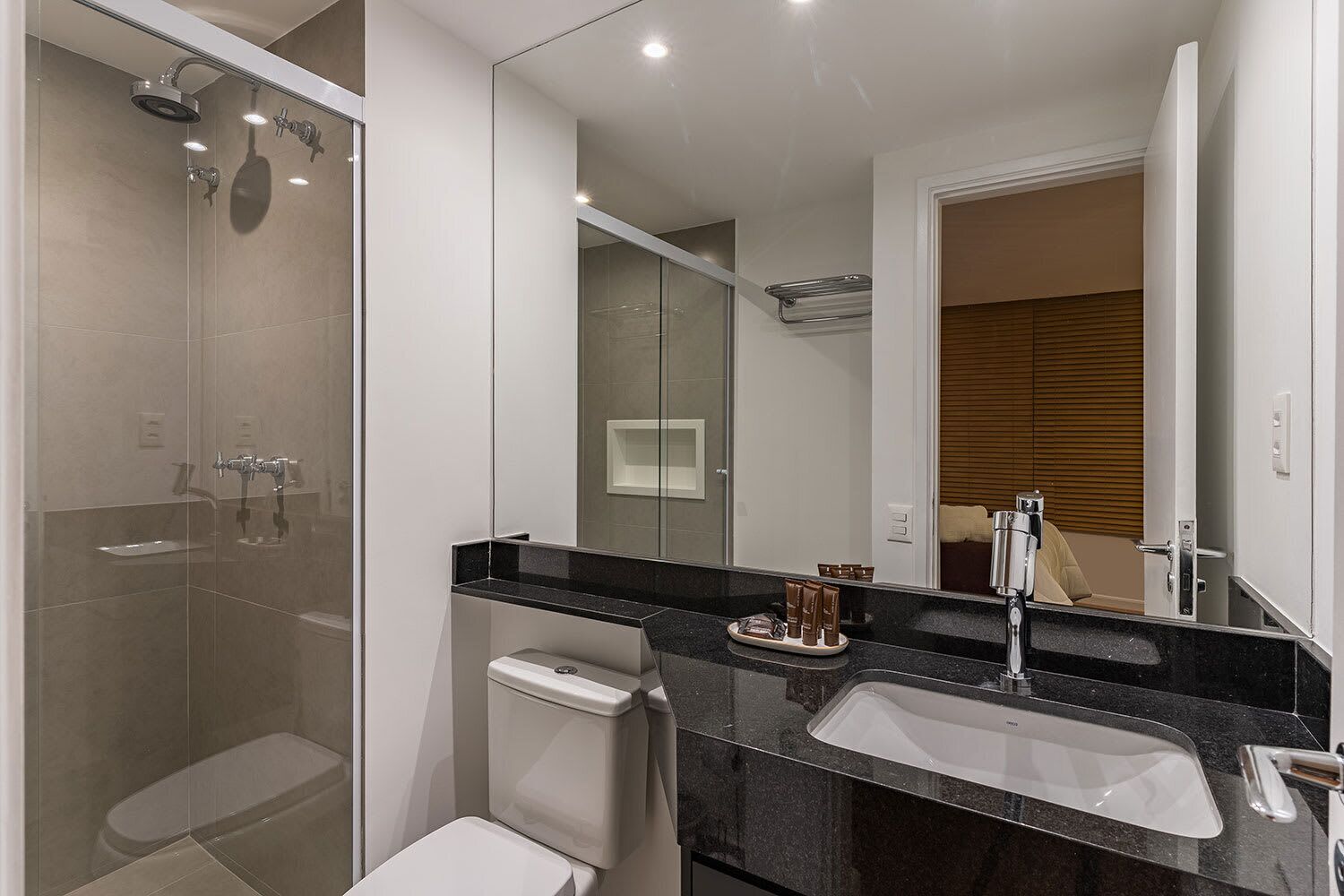 A modern bathroom with a glass shower enclosure, a white toilet, a black countertop sink, and a large mirror.