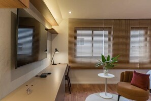 A modern living room with a sofa, a coffee table, a TV mounted on the wall, and a window with blinds. - #BC1006 | Cyclinn Bela Cintra Jardins (Bela Cintra)