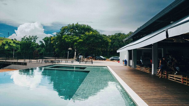 A swimming pool with a wooden deck, a covered seating area, and a view of trees and hills.