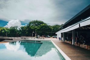 Une piscine avec une terrasse en bois, un espace salon couvert et une vue sur les arbres et les collines.