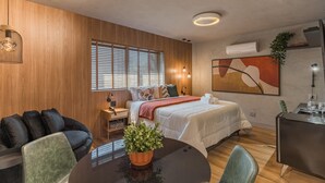 Une chambre d’hôtel moderne équipée d’un lit, d’un bureau, d’une table à manger, d’un canapé et d’une grande fenêtre avec des stores.