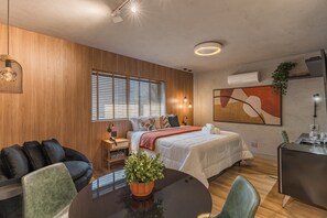 A modern hotel room with a bed, a desk, a dining table, a sofa, and a large window with blinds. - #BC802 | Cyclinn Bela Cintra Jardins (Bela Cintra)