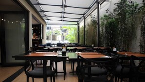 Un espace de restauration intérieur avec des tables et des chaises, de grandes fenêtres et des plantes d’intérieur.