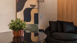 Un salon moderne avec une table en verre, un canapé foncé, une plante en pot et un mur orné d’œuvres d’art abstraites.
