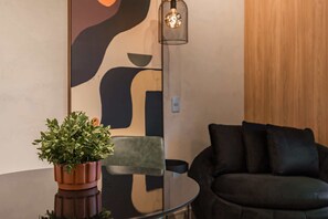 A modern living room with a glass table, a dark sofa, a potted plant, and a wall with abstract art. - #BC802 | Cyclinn Bela Cintra Jardins (Bela Cintra)