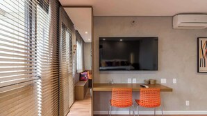 Um interior moderno com piso de madeira, área de refeições com duas cadeiras laranja, uma janela grande e uma obra de arte pendurada.