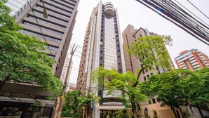 Un grattacielo con numerosi piani, circondato da vegetazione e altri edifici.