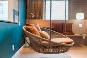 Un fauteuil suspendu en osier avec des coussins, un banc en bois et un luminaire suspendu.