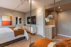Et moderne hotelværelse med seng, skrivebord, stol, fjernsyn og tekøkken.