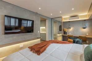 Ein modernes Schlafzimmer mit einem großen Bett, einem an der Wand befestigten Fernseher, einem Schreibtisch und einem Spiegel.