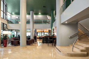 Eine großzügige Lobby mit einer geschwungenen Treppe, Sitzbereichen und einer Bar.