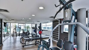 Ein modernes Fitnessstudio mit verschiedenen Trainingsgeräten, großen Fenstern und Holzboden.