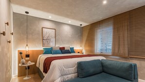 Ein modernes Schlafzimmer mit Bett, einer Couch, einem Nachttisch und einem Fenster mit Jalousien.