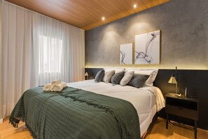 A modern hotel room with a large bed, a dark headboard, and abstract wall art. - #IN1704 | Cyclinn Jesuíno Arruda Itaim (Itaim Bibi)
