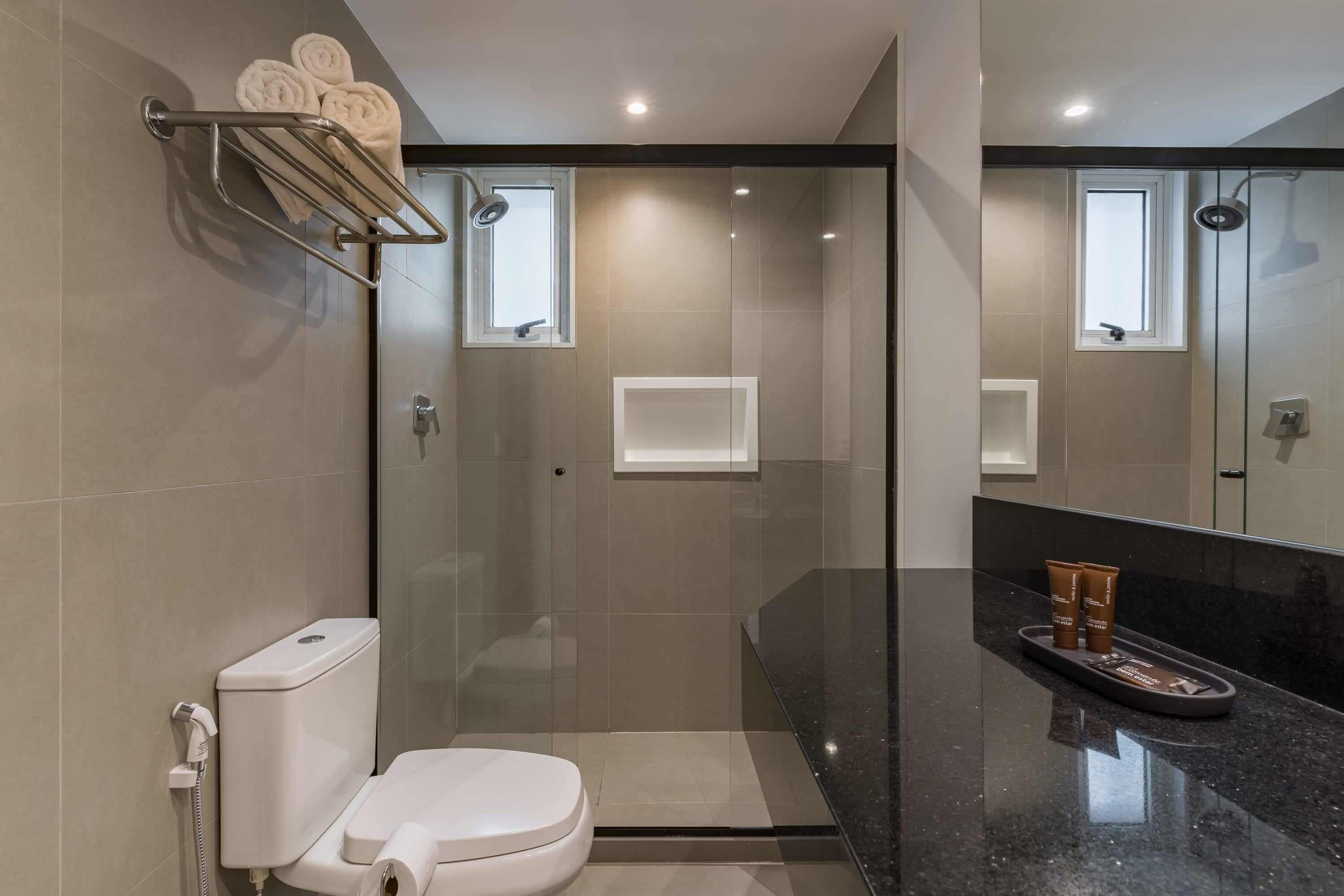 Une salle de bain moderne avec une douche à parois de verre, des toilettes, un porte-serviettes et un meuble-lavabo avec des articles de toilette.