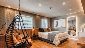 Ein modernes Schlafzimmer mit Hängekorbschaukel, einem Bett mit gemusterten Betttextilien und einem großen Fenster mit Jalousien.