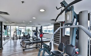 Ett modernt gym med olika typer av träningsutrustning, stora fönster och ett trägolv.