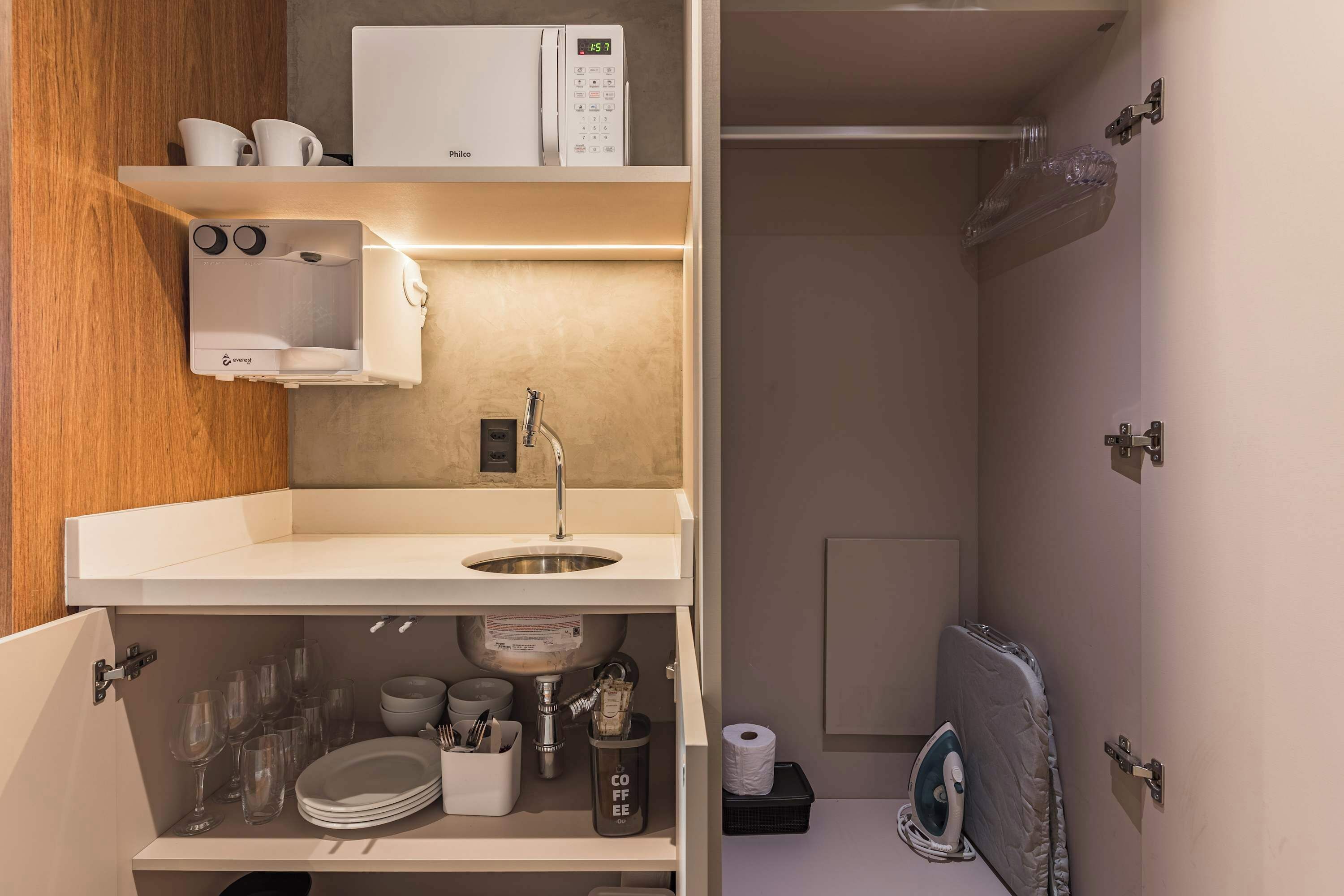 A compact kitchenette with a microwave, sink, and storage shelves.