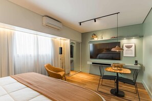 Ein modernes Hotelzimmer mit Bett, Stuhl, kleinem Tisch, Fernseher und einer Wandablage.