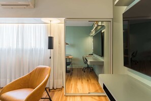 Ein modernes Zimmer mit Holzboden, einem großen Flachbildfernseher, einem bequemen Sessel und einem Schreibtisch mit Stuhl.