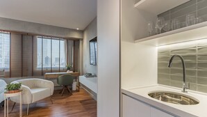 Ett modernt kök med en diskho i rostfritt stål, trägolv och en matplats med en vit soffa och ett litet bord.