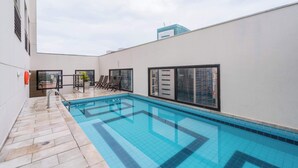 En pool på taket med kakelbeklädd botten, solstolar och utsikt över byggnaderna.