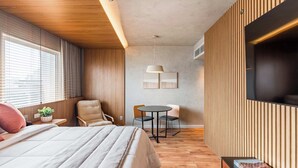 A modern hotel room with a bed, a desk, a chair, a small table, and a TV.