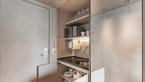 A compact kitchen with a built-in microwave, a sink, and a shelf with glasses and cups.