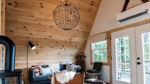 Interior acolhedor de cabana com teto de madeira, piso de pedra, um sofá, uma cadeira, uma mesa e um lustre.