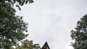 Uma cabana de madeira triangular com varanda, degraus e luzes de cordão.