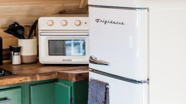 Uma cozinha com uma geladeira branca Frigidaire, uma prateleira de madeira com copos e um forno antigo.