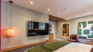 Una camera d'hotel moderna con un letto, una TV a schermo piatto, una mensola a parete, un piccolo angolo salotto e un grande quadro astratto.