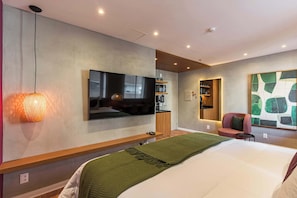 Ein modernes Hotelzimmer mit Bett, Flachbildfernseher, einer Wandablage, einer kleinen Sitzecke und einem großen abstrakten Gemälde.