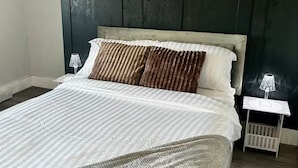 Een bed met een gestreept dekbed, twee kussens, een nachtkastje met een lamp en een wit ledikant.