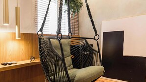 Une pièce comprenant une chaise suspendue, un banc en bois, une plante et un grand tableau abstrait.