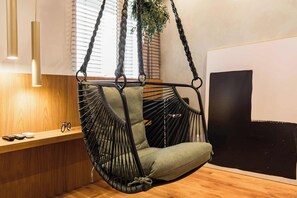 A room with a hanging chair, a wooden bench, a plant, and a large abstract painting. - #WP502 | Cyclinn Paulista Jardins (Jardim Paulista)