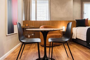 A modern hotel room with a wooden floor, a round table with two chairs, a bed with a white duvet, and a large abstract painting on the wall. - #WP501 | Cyclinn Paulista Jardins (Jardim Paulista)