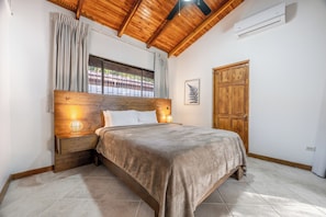 A bedroom with a wooden headboard, a bedside lamp, a window with curtains, and a door. - Casa Coco -Luxury House (Provincia de Guanacaste)