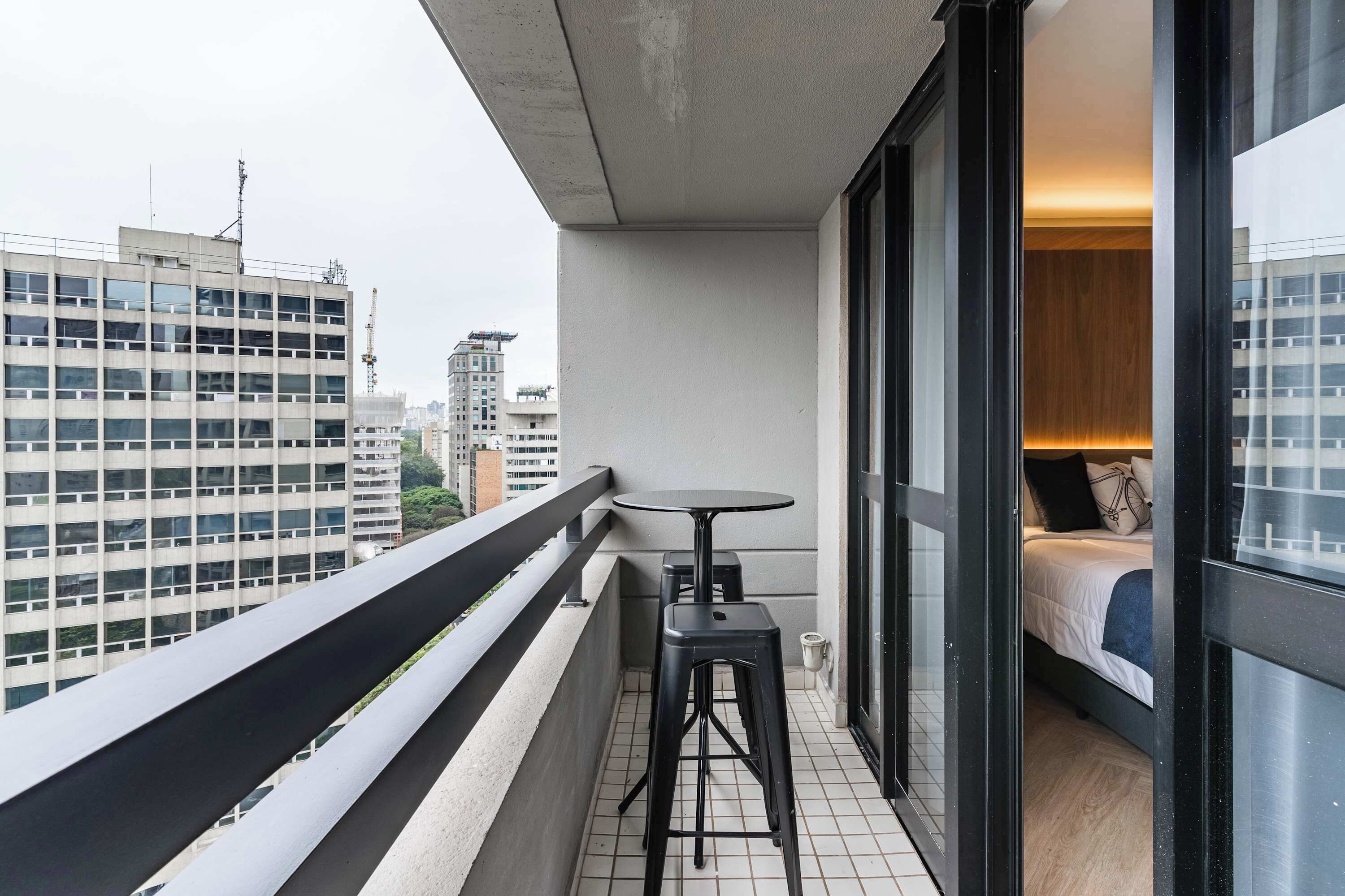 Un balcón con una mesa y taburetes, una cama con cabecera de madera y vistas a la ciudad.