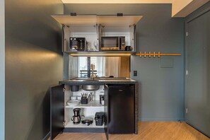 Een kleine keuken met een inbouwmagnetron, koffiezetapparaat en opbergkasten.