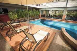 Uma área de piscina com espreguiçadeiras e um salão envidraçado.