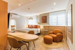Ein modernes Hotelzimmer mit Bett, Schreibtisch, Stuhl, Hocker und einem kleinen Tisch.