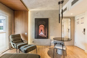 A modern room with a wooden floor, a green sofa, a round glass table, and a painting of an archway. - #VD1408 | Cyclinn Berrini Chacara Sto Antonio (Berrini)