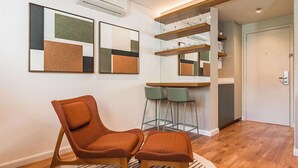 A modern room with a wooden floor, a two-seater orange chair, a round rug, and a dining area with green chairs. - Cyclinn a 400m do WTC Berrini Vila Olímpia #WB309 (Berrini)